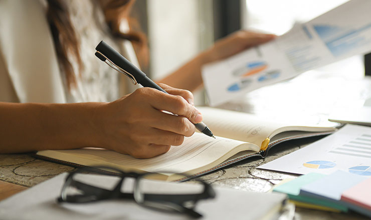 close up of person recording fixed assets on a balance sheet with a pen