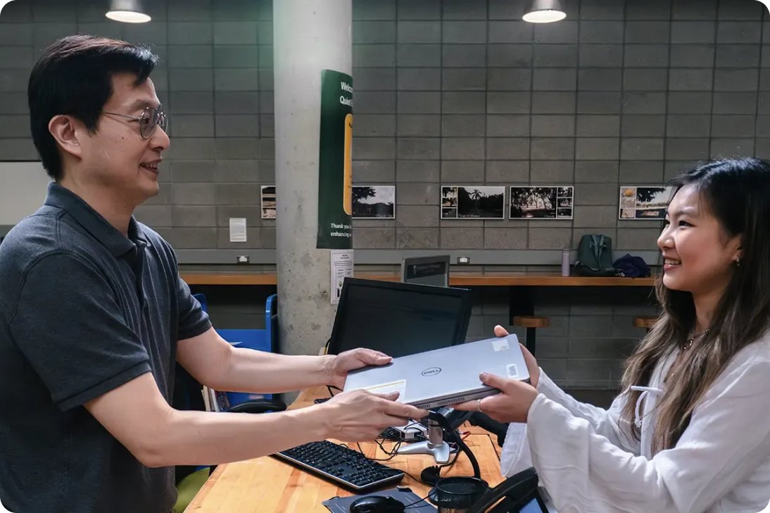 University staff member handing a laptop to a student at a campus service desk