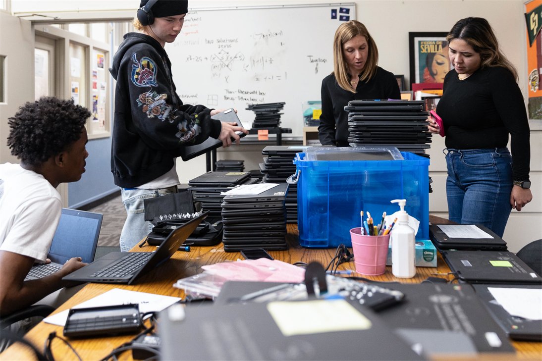 Students returning laptops and tablets to staff at a school collection desk