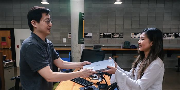 Staff handing off a laptop at a campus service desk