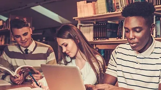 University students studying together with a laptop and books in a library