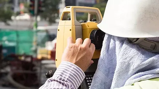 Surveyor in a hard hat operating a total station on a job site