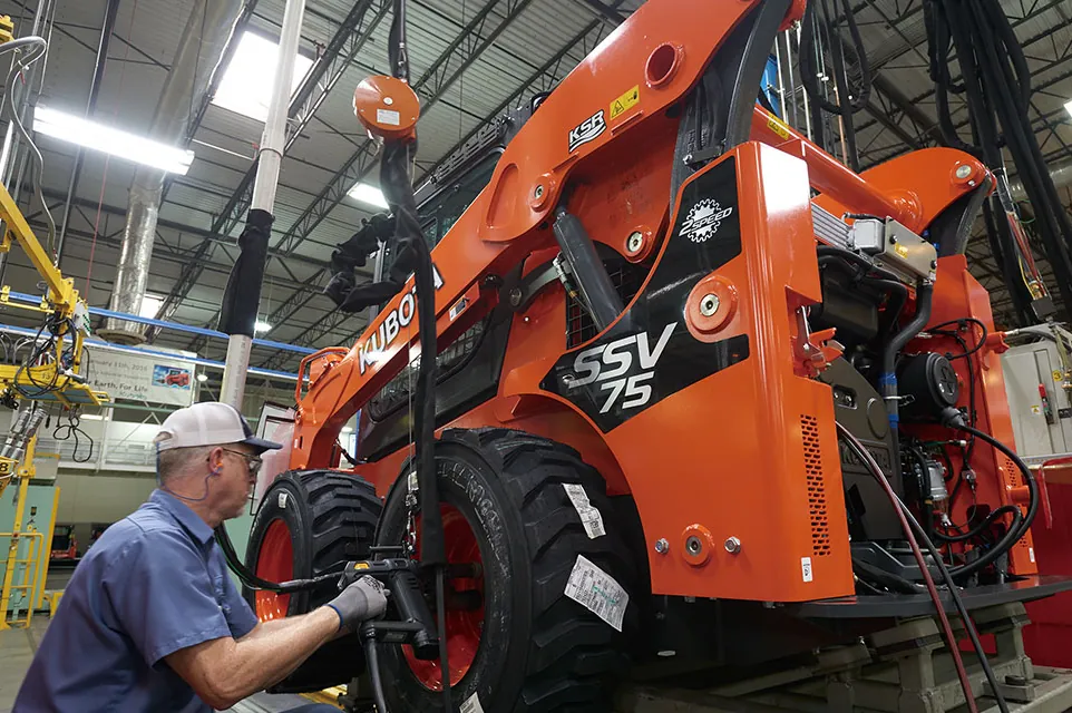 Technician servicing an orange compact track loader in a workshop