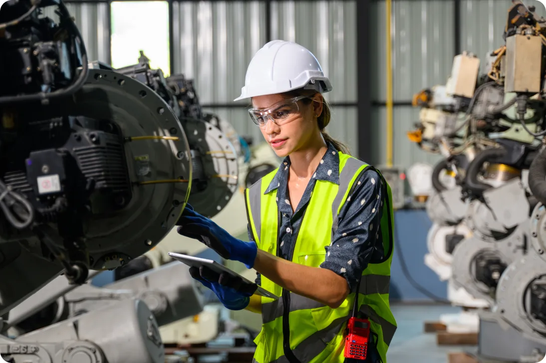 Technician in a hard hat and safety vest inspecting equipment with a tablet